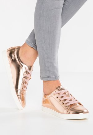 Jalat, joissa on metallinhohtoiset ruusukultaiset matalavartiset tennarit, joissa on vaaleanpunaiset nauhat ja valkoiset pohjat, yhdistettynä vaaleanharmaisiin istuviin farkkuihin.