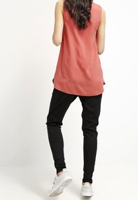 Koralfarvet ærmeløs top med en løs pasform, parret med sorte tapered bukser og hvide sneakers. Glat stof og subtile sidelæg.