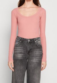 Rosa långärmad topp med scoophalsringning som kombineras med högmidjade, blekta svarta jeans med framfickor och slitdetaljer.