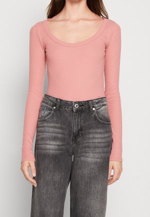 Rosa Langarmoberteil mit einem runden Ausschnitt, kombiniert mit hochgeschnittenen, ausgebleichten schwarzen Jeans, die über Fronttaschen und einen abgetragenen Look verfügen.