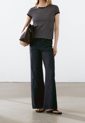 Maglietta a maniche corte a righe bianche e nere abbinata a pantaloni svasati in denim scuro a vita alta e infradito nere, con una borsa nera dalla trama evidente in mano.