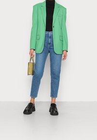 Mintgrön blazer med en enda knapp, kombinerad med högmidjade blå jeans och svarta plattformsskor. Håller en liten olivgrön väska.