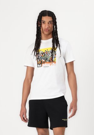 Witte katoenen t-shirt met een kleurrijke grafische print aan de voorkant, gecombineerd met zwarte shorts en een gele logo-accent op de tailleband.