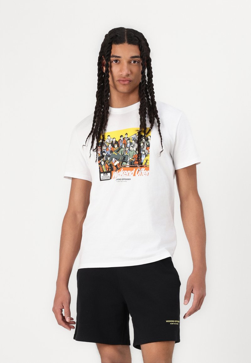 White cotton t-shirt featuring a colorful graphic print on the front, paired with black shorts and a yellow logo accent on the waistband.