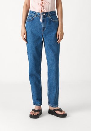 Blauwe high-waisted jeans met een rechte pijp, gemaakt van denim, met zijzakken en subtiele stiksels. Gecombineerd met zwarte teenslippers.
