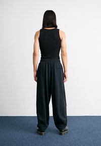 Svart ribbad tank top i kombination med löst sittande, mörka byxor med elastisk midja och sidficka, bärs med kraftiga svarta kängor.