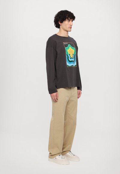 Zwarte langmouwen shirt met kleurrijk geometrisch ontwerp, gecombineerd met beige broek en witte sneakers. Casual pasvorm met een relaxte silhouet.