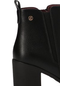 Botín negro de cuero hasta el tobillo con un acabado texturizado, paneles laterales elásticos y un tacón grueso. Cuenta con un pequeño acento de logo metálico.