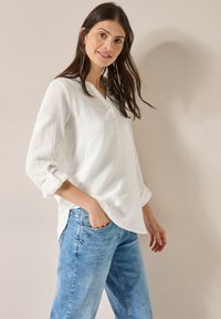 Hvid struktureret skjorte med oprullede ærmer, parret med lyseblå denim jeans. Skjorten har en afslappet pasform og en krave.