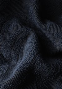 Tissu en bleu marine texturé présentant un motif ondulé, mettant en valeur une surface douce et moelleuse avec des crêtes surélevées et des détails complexes.