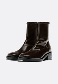 Bottes courtes en cuir marron avec fermeture éclair, bout arrondi et talon bloc. Présentent une texture lisse et des coutures ton sur ton le long des coutures.