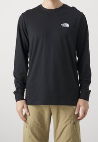 Schwarzes langärmliges T-Shirt aus Baumwolle mit Rundhalsausschnitt und Logodetail auf der linken Brust, mit gerippten Bündchen.