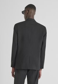 Crni krojeni sako s jednim prorezom, dugim rukavima i zakopčanim manžetama, s dizajnom koji se odlikuje glatkom teksturom i strukturiranim oblikom.