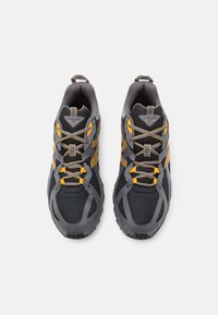 Szare buty sportowe z żółtymi akcentami, posiadające siateczkową cholewkę, wyściełany kołnierz i grubą gumową podeszwę. Obecny szczegółowy system sznurowania.