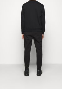 Sudadera y pantalones negros, ambos de tela lisa, con un diseño sencillo que incluye puños y cintura acanalados. Zapatillas negras completan el conjunto.