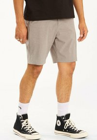 Pantalones cortos grises de tela texturizada, hasta la rodilla, con bolsillos laterales. Llevados con zapatillas altas negras y calcetines blancos.