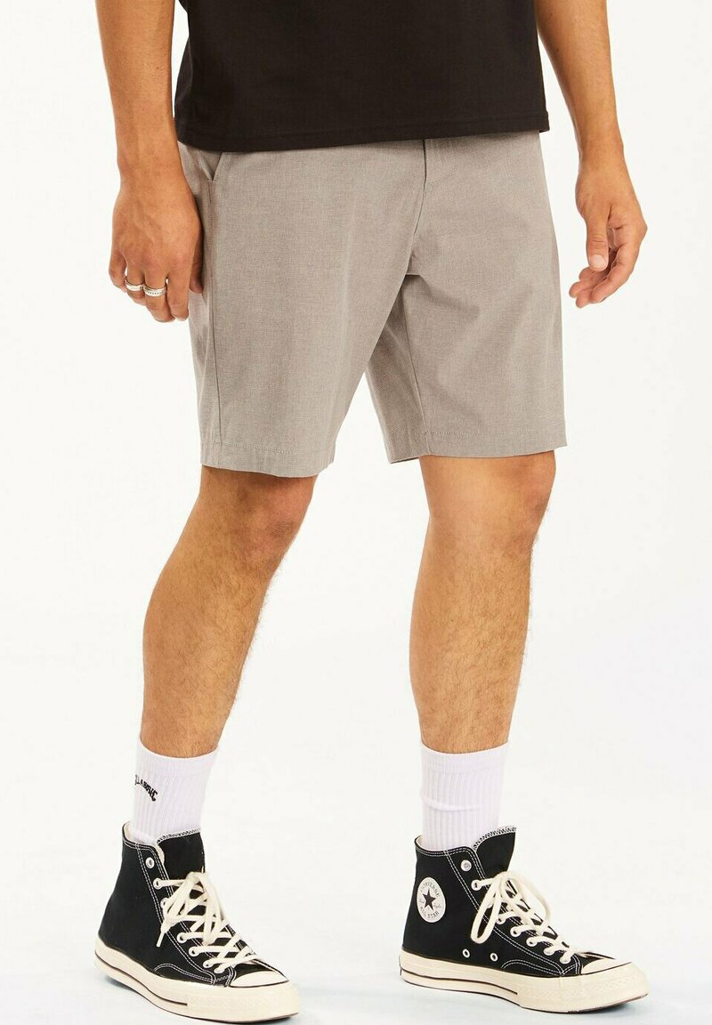 Pantalones cortos grises de tela texturizada, hasta la rodilla, con bolsillos laterales. Llevados con zapatillas altas negras y calcetines blancos.