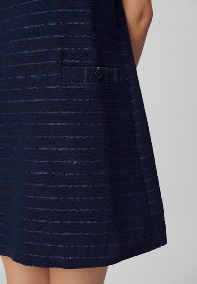 Vestido azul marino con rayas horizontales texturizadas y lentejuelas, bolsillo lateral con detalle de botón y forma suelta en A.