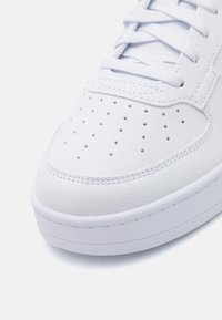 Weiße Ledersneaker mit perforierter Zehenpartie, glatter Oberfläche und flachen weißen Schnürsenkeln. Die Sohle ist aus Gummi mit einem dezenten erhöhten Rand.
