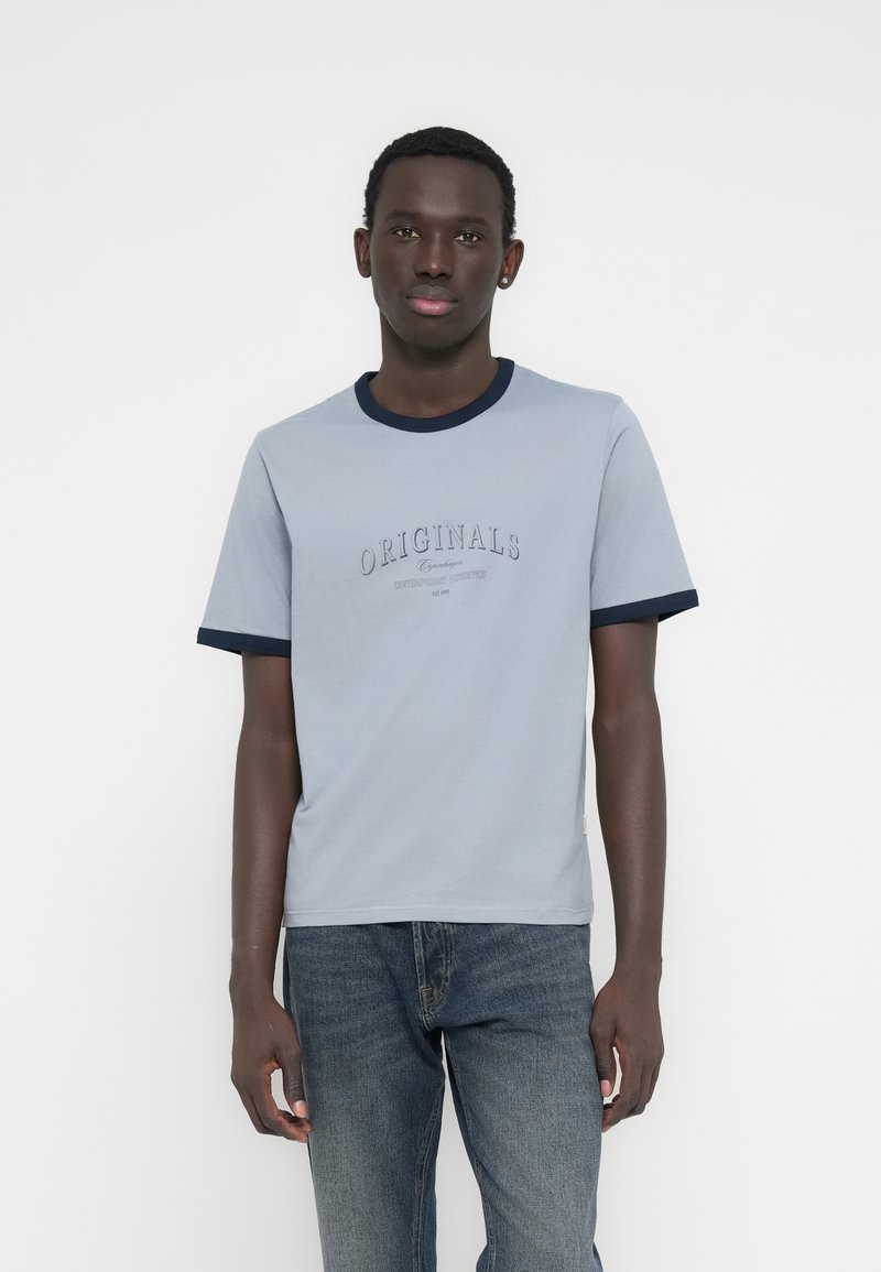 Ανοιχτό μπλε μπλουζάκι με σκούρο μπλε ριμπ λαιμόκοψη και μανσέτες, με κεντημένο το κείμενο «ORIGINALS» στο στήθος. Ομαλό βαμβακερό ύφασμα.