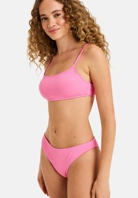 Roza bikini komplet iz teksturirane tkanine, ki ima tanke naramnice in obliko triangel bralette ter ujemajoče se kratke hlače z visokim pasom.