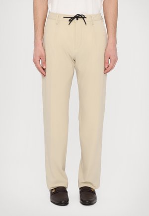 Beige broek gemaakt van lichte stof met een trekkoord in de taille. Beschikt over twee zakken aan de voorkant en een rechte pasvorm.