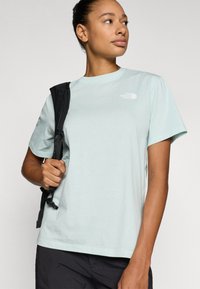 Ανοιχτό μπλε κοντομάνικο μπλουζάκι από απαλό ύφασμα. Έχει μικρό λευκό λογότυπο στο στήθος και χαλαρή εφαρμογή, συνδυασμένο με μαύρο σακίδιο.