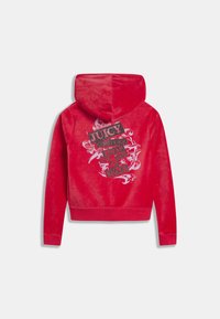 Piros bársonyos kapucnis pulóver, melyen fekete és ezüst kiemelésekkel ellátott "JUICY" felirat és díszítő hullám minták találhatók a hátoldalon.