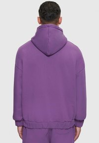 Lila Kapuzenpullover mit einer großen Kapuze, gerippten Bündchen und Saum. Glatte Textur, lässige Passform, sichtbare Nahtdetails.