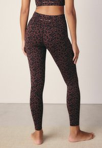 Leggings taille haute d'un bordeaux foncé avec un motif léopard noir. Fabriqués dans un matériau lisse et extensible, ils présentent des coutures plates.