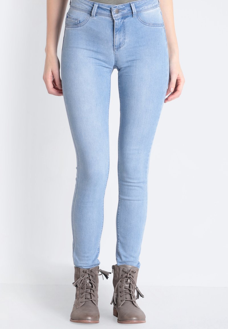 Jeans ajustados de color azul claro, fabricados en denim, con cintura alta, cinco bolsillos y una textura suave, combinados con botas de tobillo gris con cordones.