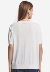 Top in maglia bianca a maniche corte con vestibilità ampia, scollo rotondo e dettagli a costine sull'orlo e sui polsini, che mostrano una texture liscia.