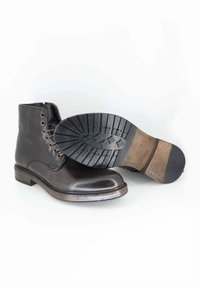 Stivali ankle in pelle marrone con occhielli metallici e lacci, suola in gomma piatta con motivo di battistrada, finitura liscia e accentuazione del tallone in contrasto.