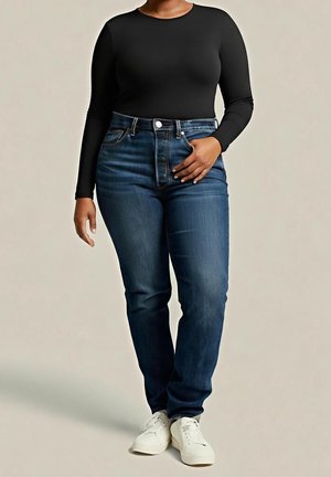 Femme portant un haut noir à manches longues, un jean taille haute bleu foncé et des baskets blanches, debout avec une main sur la hanche.