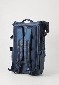 Dunkelblauer Rucksack mit gepolsterten Schulterträgern, Seitentaschen, einem Rolltop-Design und verstellbaren Beschlägen für einen sicheren Sitz.