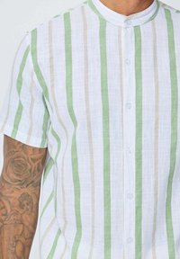 Chemise à manches courtes en lin l éger, présentant un tissu blanc avec des rayures verticales vertes et beiges, col rond et texture subtile.