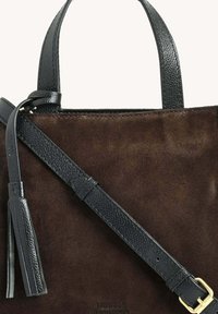 Sac fourre-tout en suède marron avec des poignées en cuir noir texturé et une bandoulière détachable. Présente une boucle en métal doré et un détail de frange.