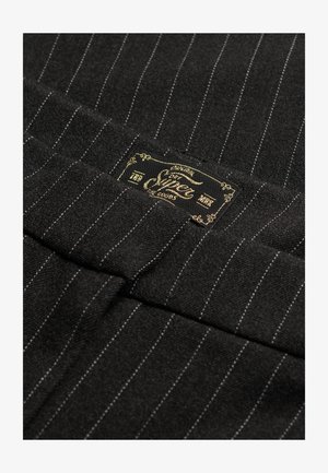 Un tissu noir avec des rayures blanches, texture douce, et une étiquette dorée et noire brodée sur le bord supérieur.