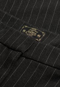 Tessuto nero a righe sottili con una sezione piegata e una piccola etichetta rettangolare per abbigliamento nera e dorata.