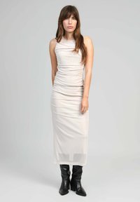 Robe sans manches, beige clair, ajustée avec une texture froncée, atteignant le mollet, associée à des bottes noires jusqu'aux genoux. Design simple.