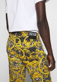 Bleka denimjeans med ett svart och gult barocktryck. Har en svart etikett med "VERSACE JEANS COUTURE" på baksidan.