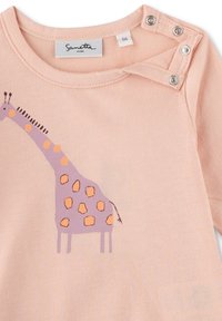 Helles rosa Langarmhemd mit einem lila Giraffenmotiv, das orangefarbene Flecken zeigt. Druckknöpfe an der Schulter verbessern die Zugänglichkeit.