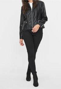 Veste en cuir noir avec une fermeture éclair à l'avant, deux poches zippées et une texture lisse. Associée à un pantalon noir et des bottines.