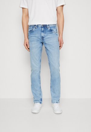 Light blue denim jeans with a straight leg design, five-pocket styling, and a faded finish. Paired with a white T-shirt and white sneakers.