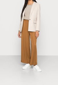 Blazer beige con bottone singolo, maglietta a righe, pantaloni larghi marroni e sneaker bianche. Design semplice con linee pulite e morbide trame.