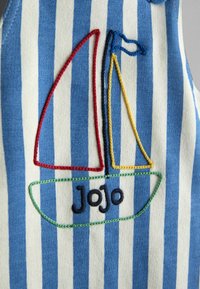 Pamut ruhadarab kék-fehér függőleges csíkokkal. Hímzett vitorlás motívum piros, sárga és zöld díszítéssel, valamint "Jojo" felirattal.