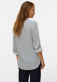 Chemise à rayures à manches longues en bleu clair et blanc, avec des manches retroussables, des accents de bouton et un ourlet incurvé. Fabriqué en tissu léger.