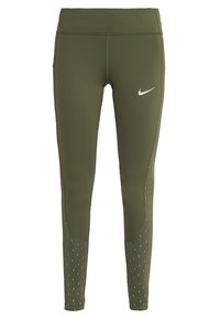 Oliwkowe legginsy sportowe z wysokim stanem, z odblaskowym logo Nike, teksturowymi akcentami oraz kropkowanymi wzorami po bokach.
