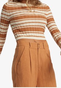 Sweter w pomarańczowo-kremowe paski, skrócony, wykonany z dzianiny; połączony z wysokim stanem, teksturowanymi spodniami w kolorze rdzy, z dwoma guzikiem z przodu.