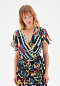 Robe portefeuille avec un haut à rayures multicolores et des manches flottantes, se transformant en une jupe à motifs floraux aux couleurs vives sur un fond sombre.